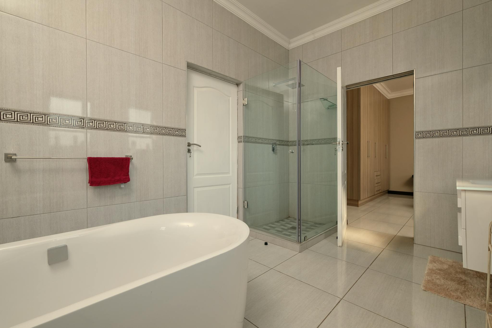 Spacious modern bathroom featuring a white bathtub, glass shower, and elegant tiled walls.